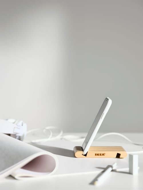 Un prim-plan al spațiului de lucru al unui suport bej pentru telefon mobil sau tabletă din bambus, amplasat pe o suprafață albă.