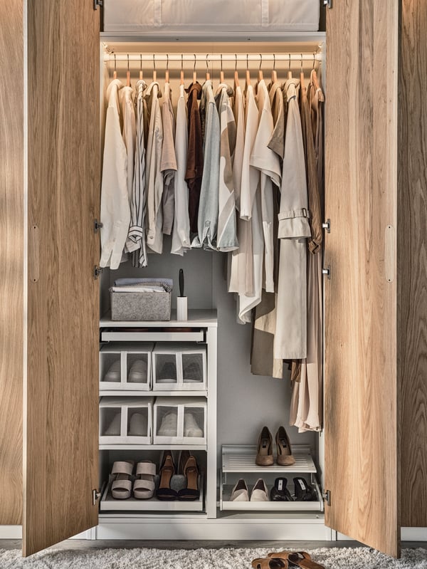 An open PAX/TONSTAD wardrobe with a KOMPLEMENT hanging rail holding shirts and coats and a KOMPLEMENT frame divider below.