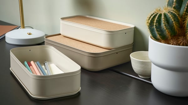 A desk with a light beige HARVMATTA box with lid and a box filled with pencils.