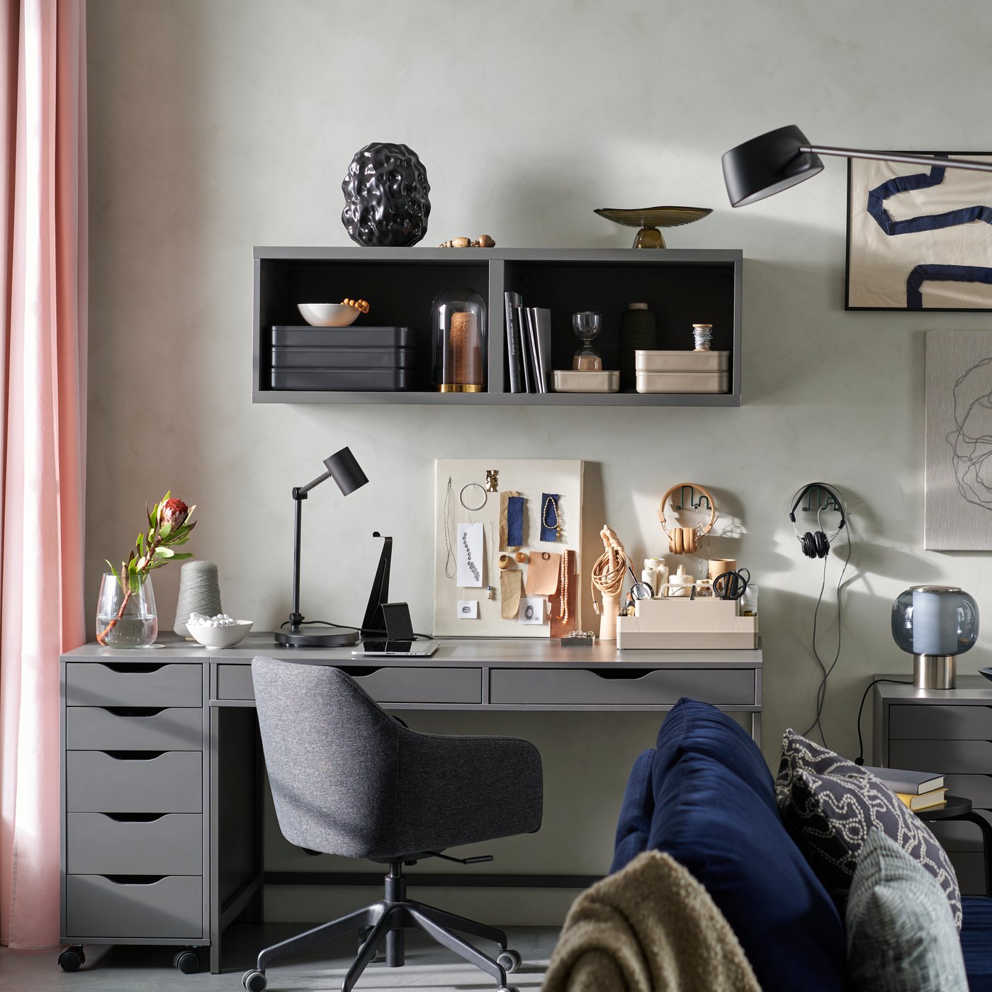 Ett vardagsrum med soffa, konstvägg och en hobbyhörna som skapats med ALEX av mörkgrå skrivbords- och förvaringsmöbler.