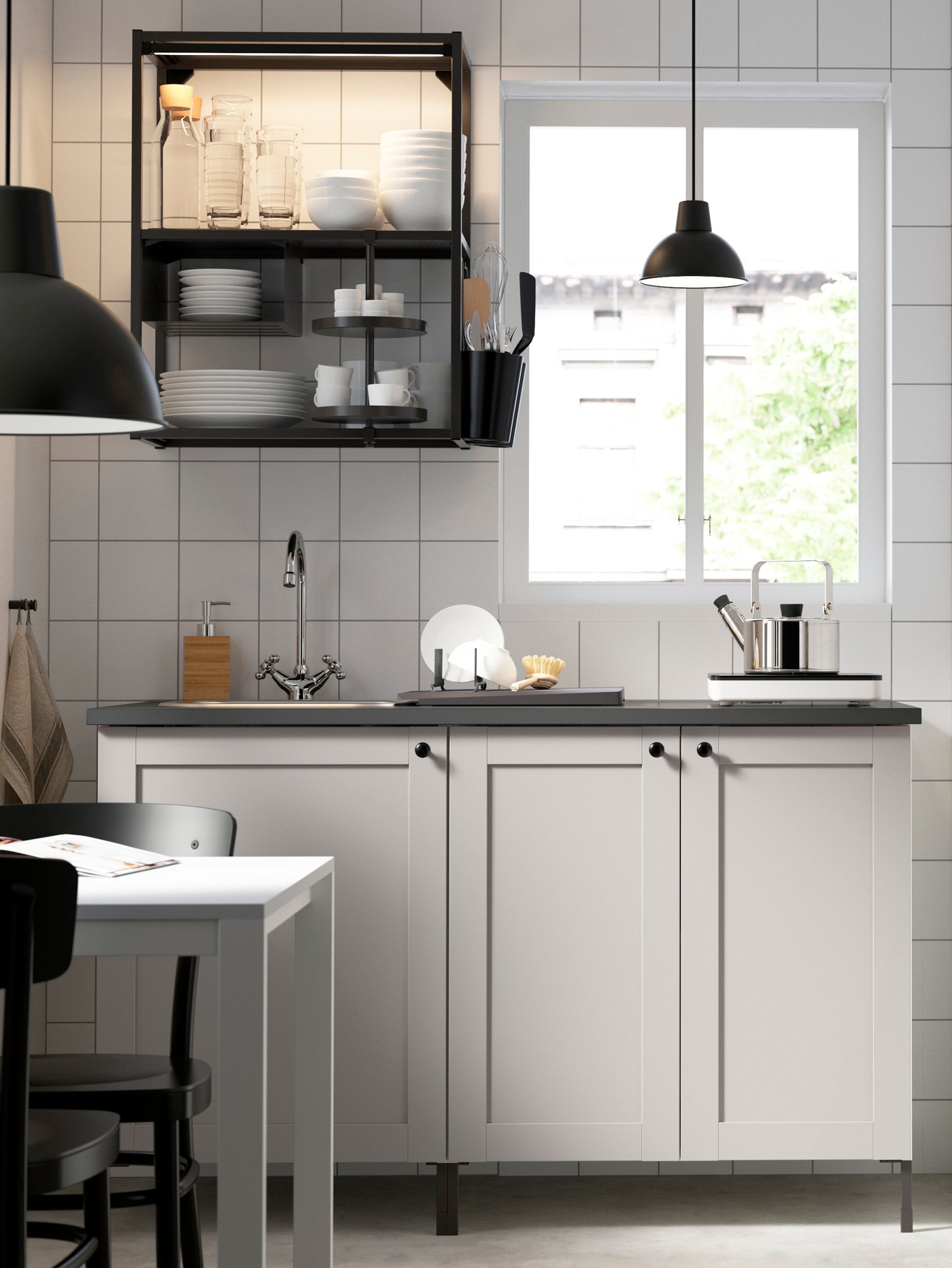 Una cocina luminosa con azulejos blancos, una cocina ENHET con frentes blancos y estanterías negras junto a una ventana. 
