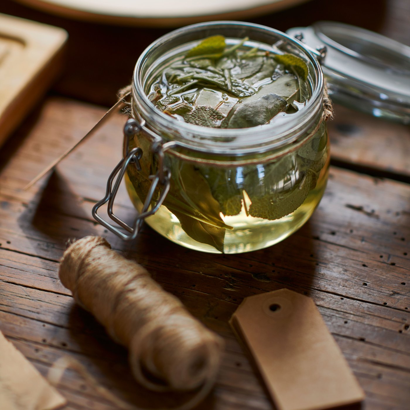 A small KORKEN jar, with the lid open, containing herbs and liquid, is placed on a wooden surface, next to a ball of string.
