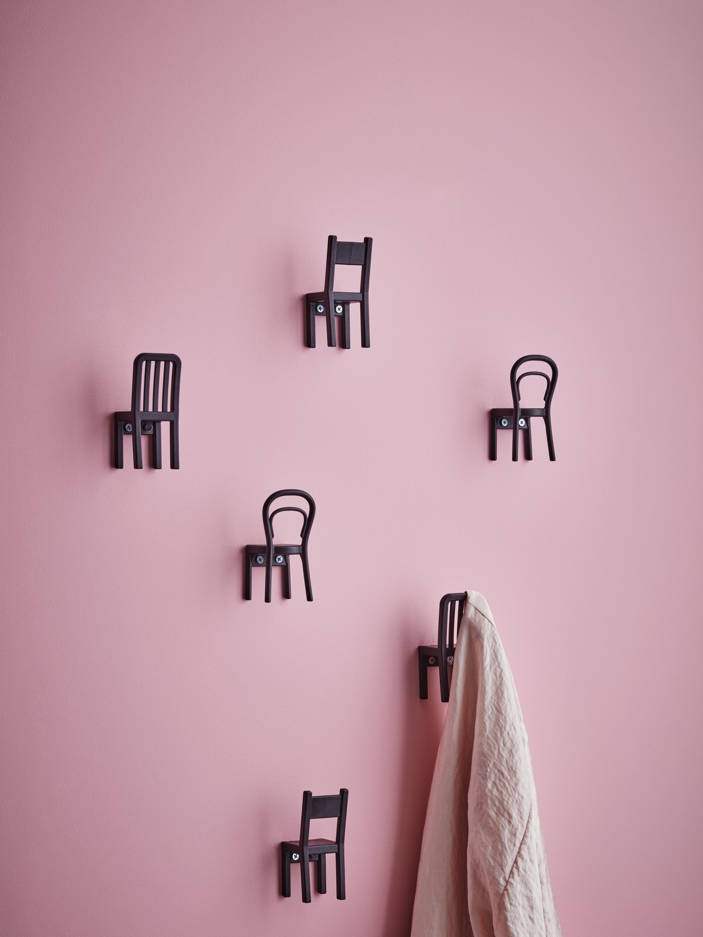 Pared rosa con seis ganchos de plástico con forma de sillas, de una de ellas cuelga un pañuelo blanco.