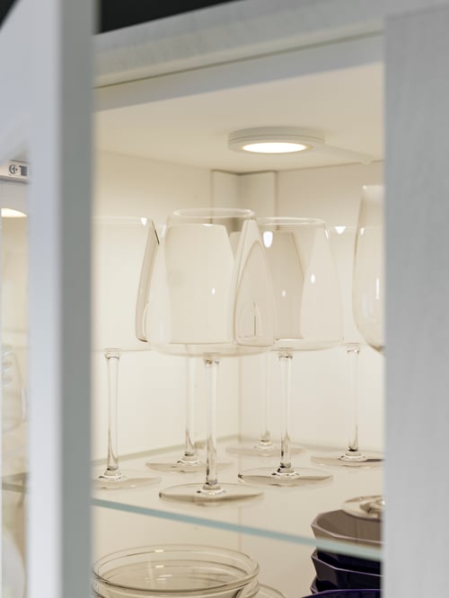 Nahaufnahme eines Schranks mit Vitrinentüren, in dem DYRGRIP Rotweingläser stehen. Sie werden von einem MITTLED LED-Spot angeleuchtet.
