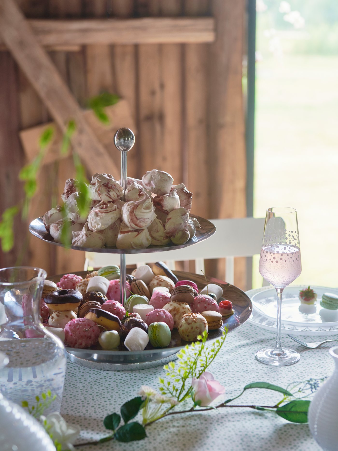 O femeie ține un platou INBJUDEN și oferă o selecție de dulciuri unui invitat la nuntă, într-un cadru rustic.