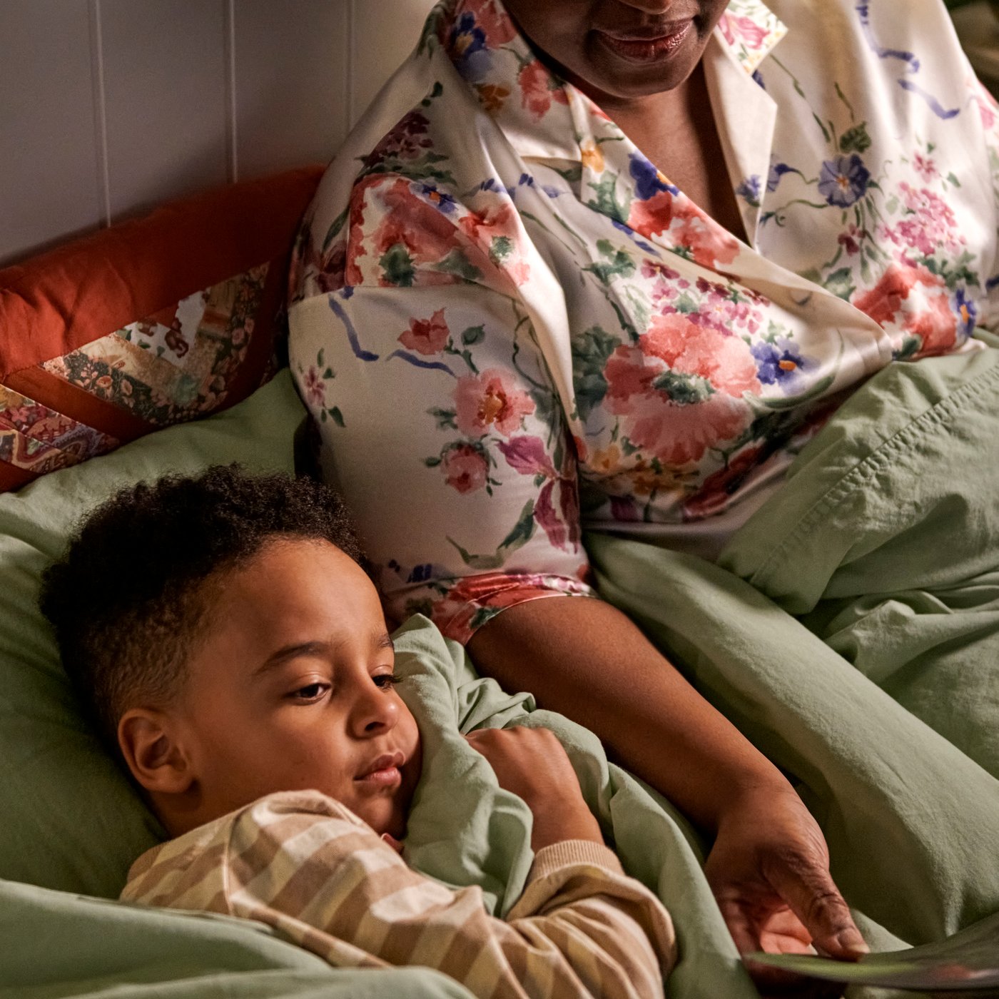 Un bambino e un adulto condividono un copripiumino e una federa ÄNGSLILJA di colore grigio-verde chiaro mentre leggono un libro a letto.