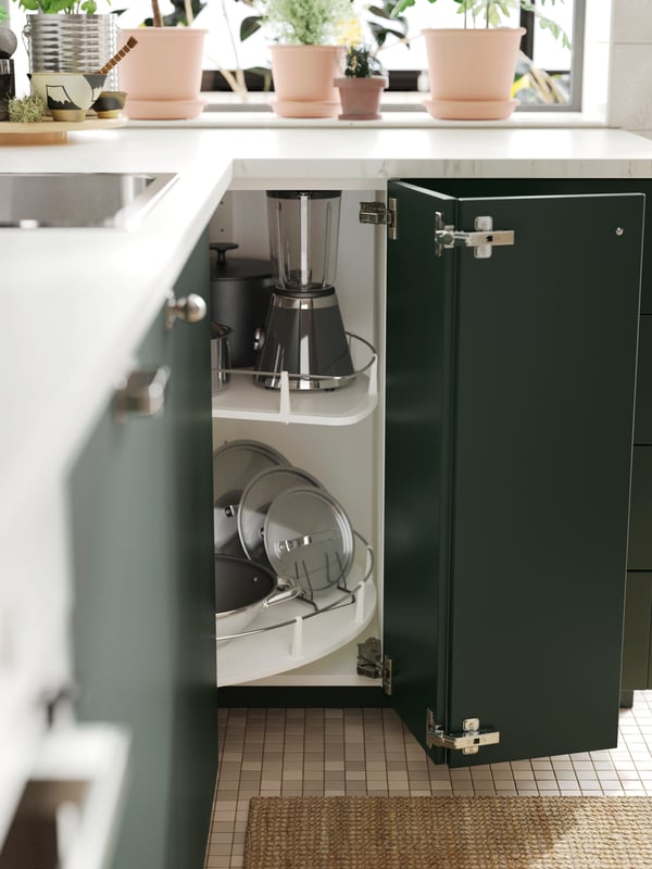 A cabinet with deep green kitchen fronts and doors open, showing an UTRUSTA corner base cabinet carousel with various items.