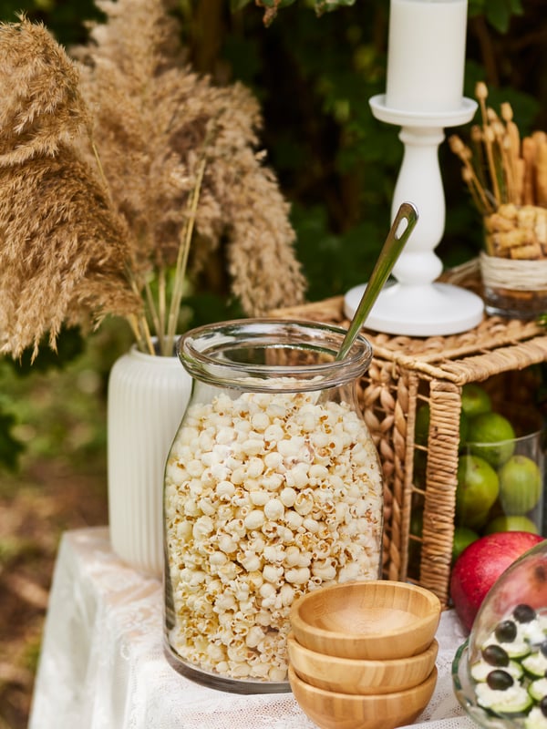 Un grand bocal de stockage avec du pop-corn et une cuillère de service. A côté, il y a des bols en bois.