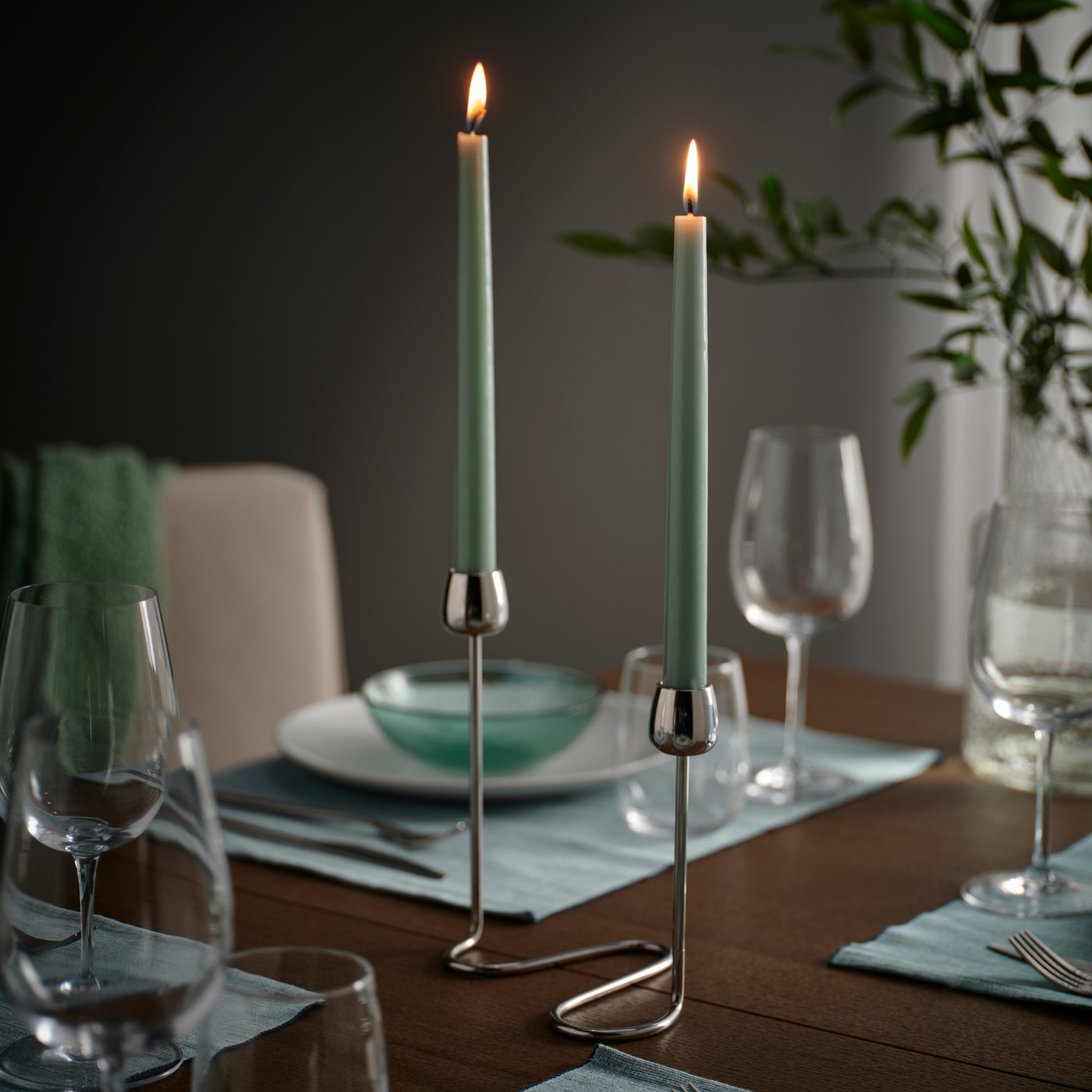 Elegant dining table with candles, blue place mats, white plates, green bowls, and cozy decor in a modern setting.