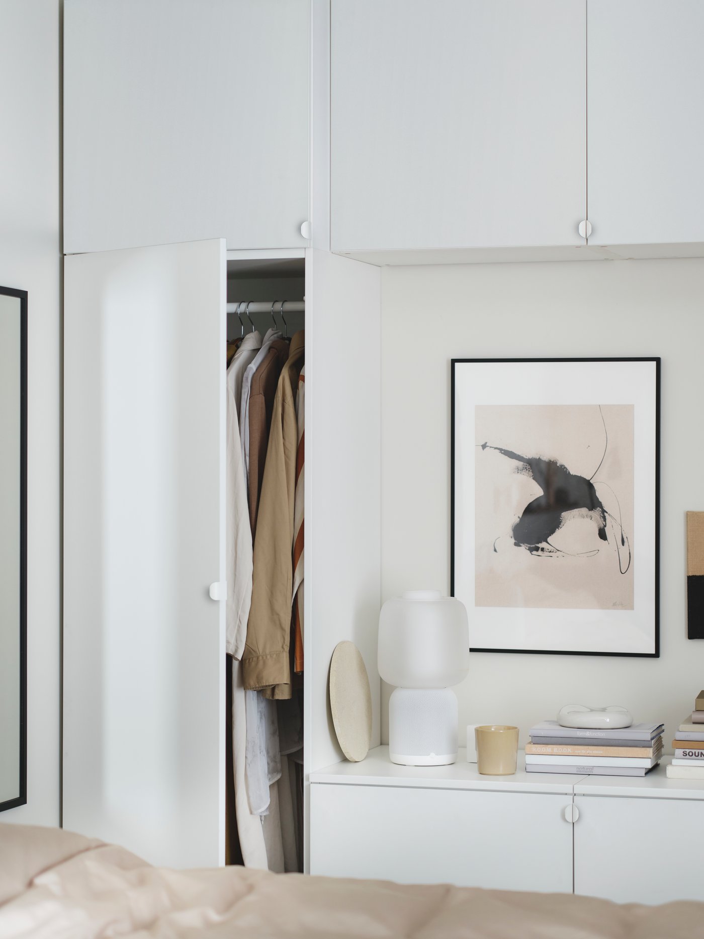 A PLATSA wardrobe combination in white with an open door filled with clothes. A mirror and a lamp are placed next to it.