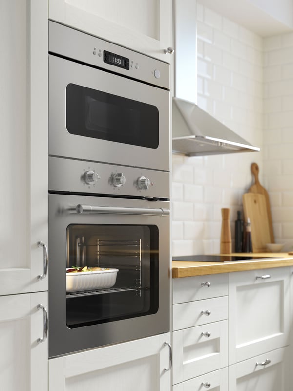 A MATTRADITION forced air oven in stainless steel is mounted in a bright white kitchen and it has a casserole cooking inside.