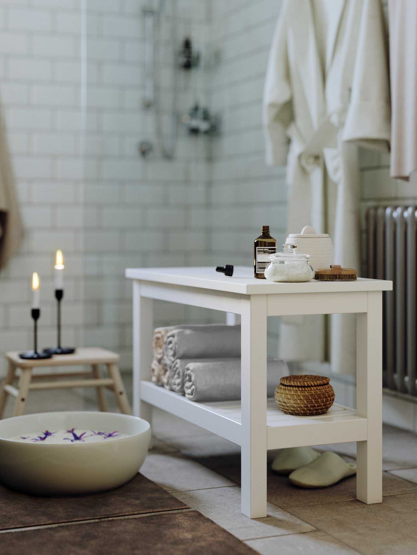 HEMNES bænk står i badeværelse med sterinlys, fodbad og håndklæder ligger på hylden. 