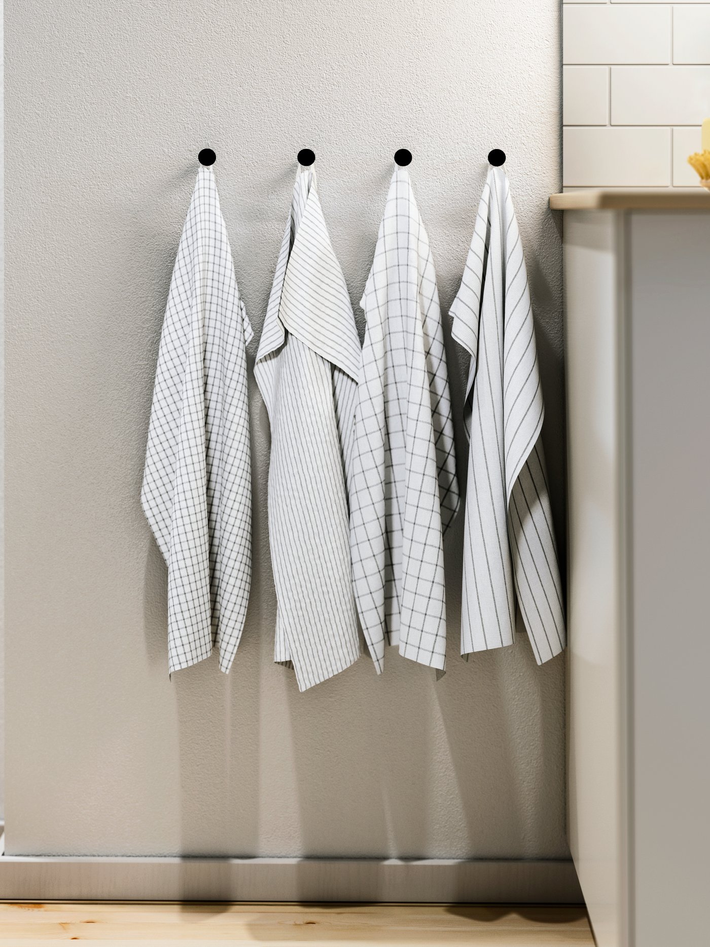 Vaalealla seinällä on neljä mustaa nuppia, joihin on ripustettu RINNIG-keittiöpyyhkeitä.