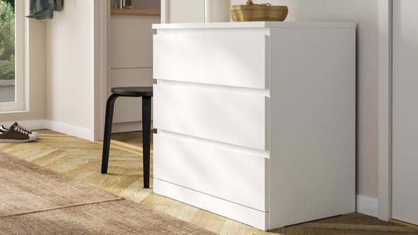 Cómoda blanca MALM con tres cajones junto a pared blanca.