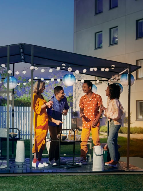 RUNNEN/ルッネン 屋外用フロアデッキ、太陽電池式LEDランプを設置したGUNNÖN/グンノン ガゼボで、夜に屋外で交流する2組のカップル。