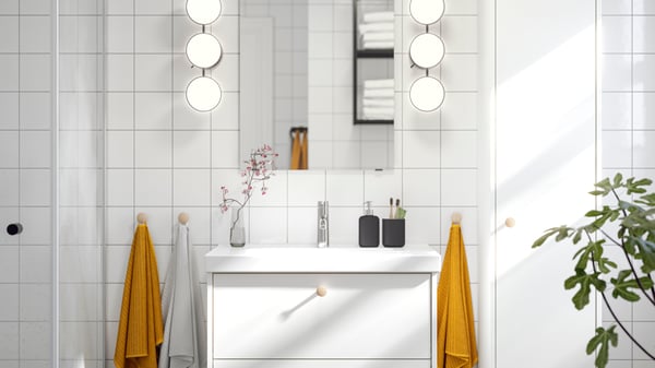 A LETTAN mirror with KABOMBA LED wall lamps on either side of it is placed above a white HAVBÄCK wash-stand with two drawers.