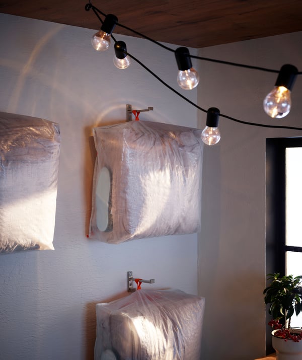PÄRKLA storage bag hanging on a wall with cushions inside. 