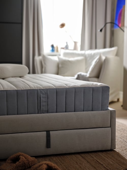 O saltea cu arcuri împachetate VALEVÅG așezată pe un pat tapițat cu o pernă ergonomică deasupra, într-un decor modern de dormitor.