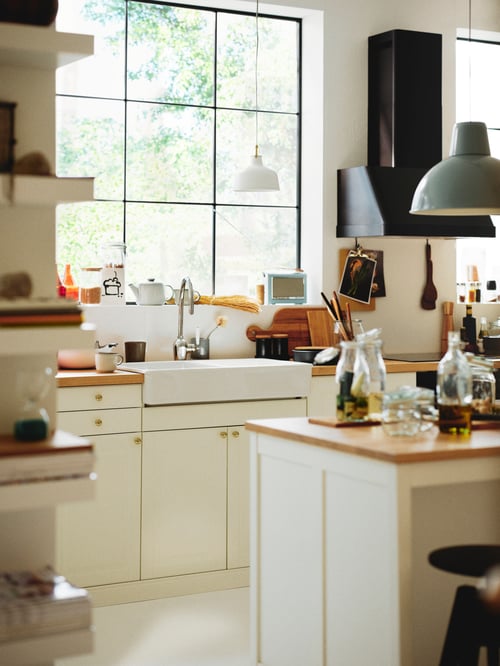 A kitchen with white cabinets with BODBYN doors, a sink with a mixer tap, and an extractor hood and pendant lamp above.