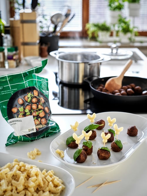 A bag of HUVUDROLL vegetable balls beside a plate of vegan meatball appetisers; a frying pan contains more in the back.