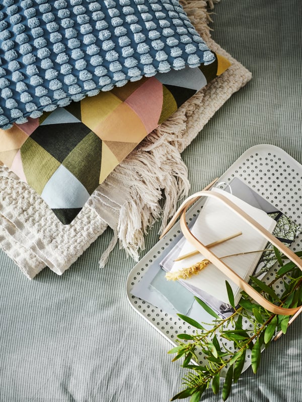 A pile of bed linen on BERGPALM bed linen includes cushions in a multicolour SVARTHÖ cover and a pale blue SVARTPOPPEL cover.