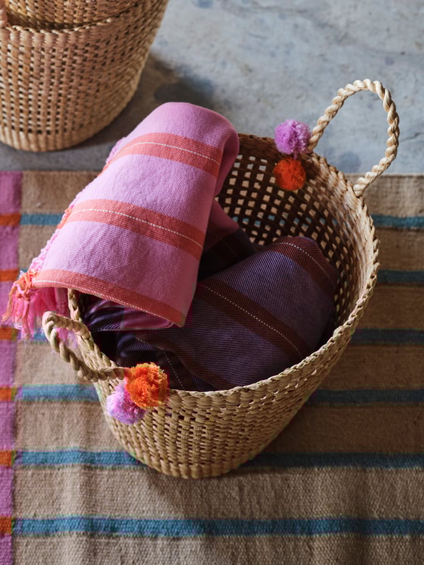Coperta MÄVINN in un cesto intrecciato MÄVINN su un tappeto MÄVINN