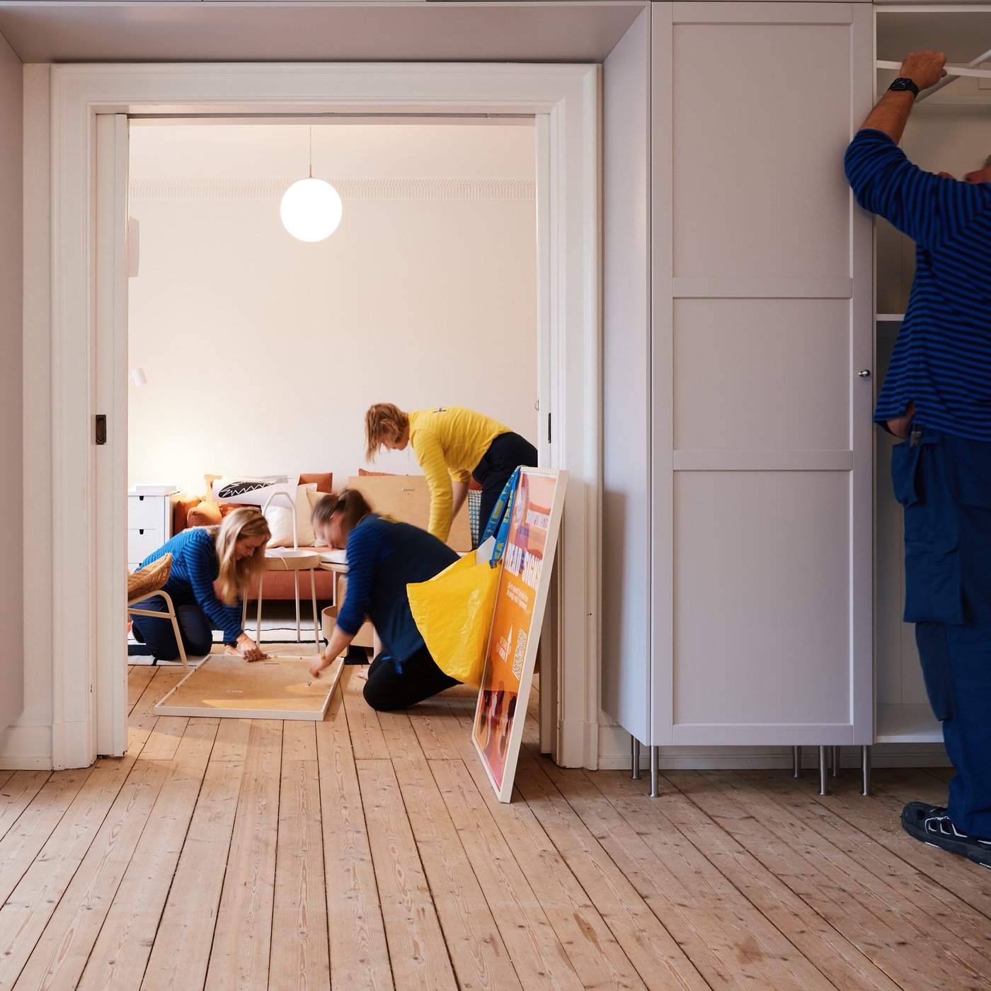 Flere mennesker fra IKEA Naboskab i gule og blå IKEA trøjer bygger møbler i en tom lejlighed