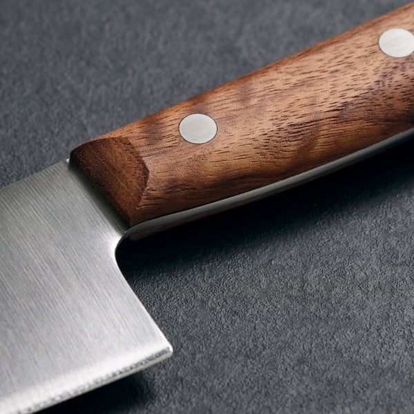Ein VARDAGEN Küchenmesser mit Edelstahlklinge und Holzgriff mit Metallnieten liegt auf einer dunklen Oberfläche.