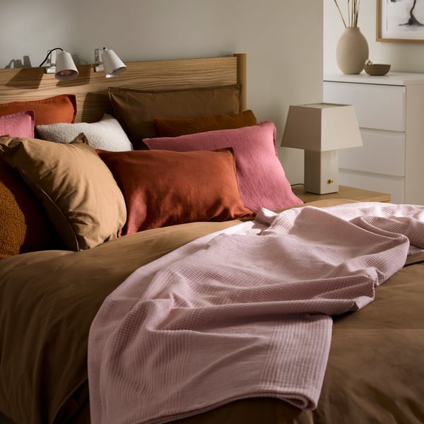 A bedroom with a bed covered in a mix of pink and brown cushions, featuring a soft pink throw, creating a cosy atmosphere.