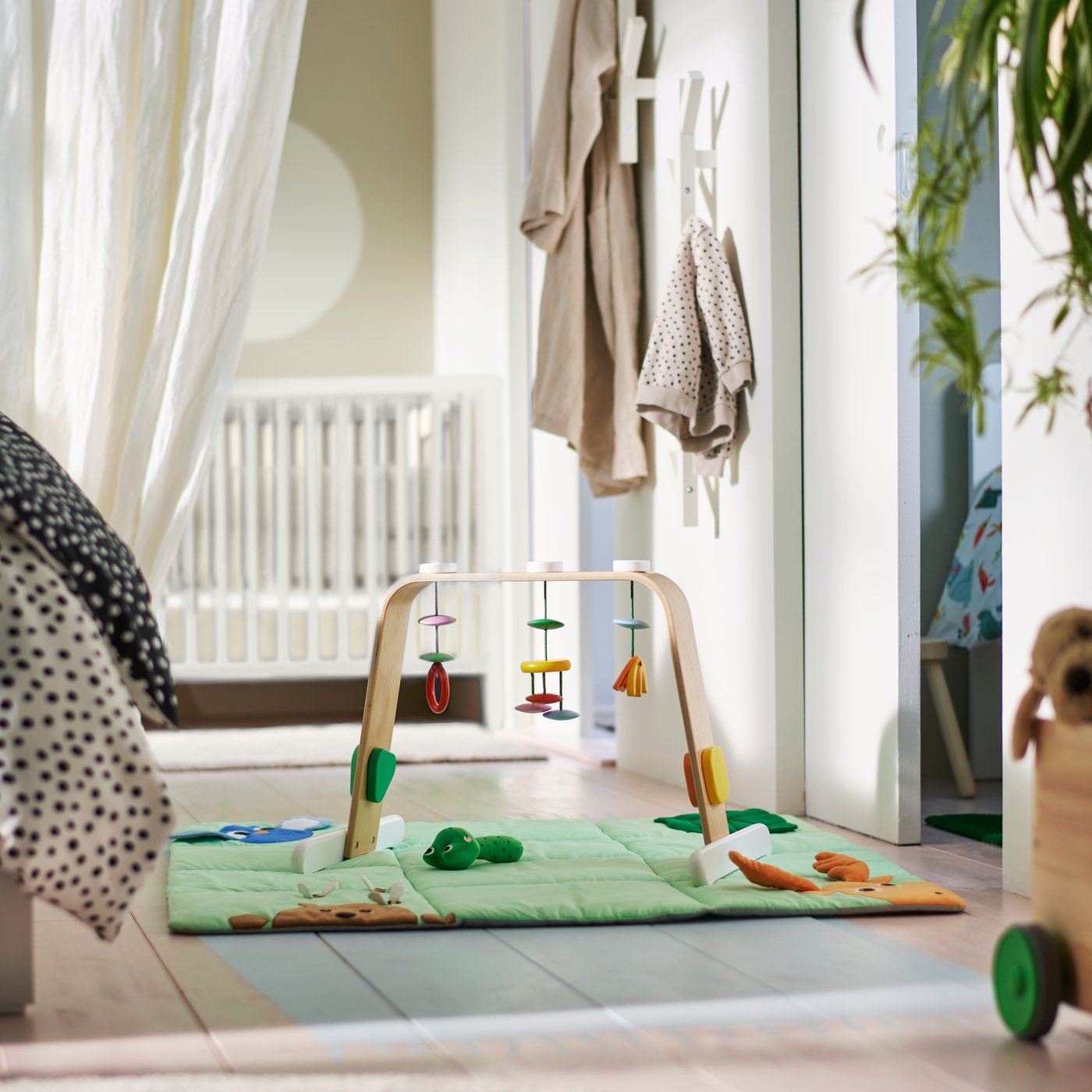 A LEKA baby gym on a green mat in a white and beige children’s room.