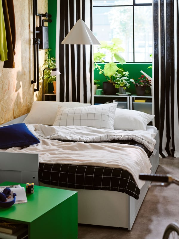 Una cama de día BRIMNES gris con 2 cajones abierta como cama doble, con un juego de edredón VITKLÖVER de cuadros blancos/negros encima.