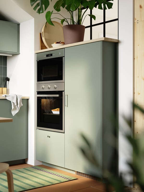 Une cuisine est équipée d'armoires de cuisine avec des façades NICKEBO gris vert, d'un four encastré, d'un four micro-ondes et d'un réfrigérateur/congélateur.