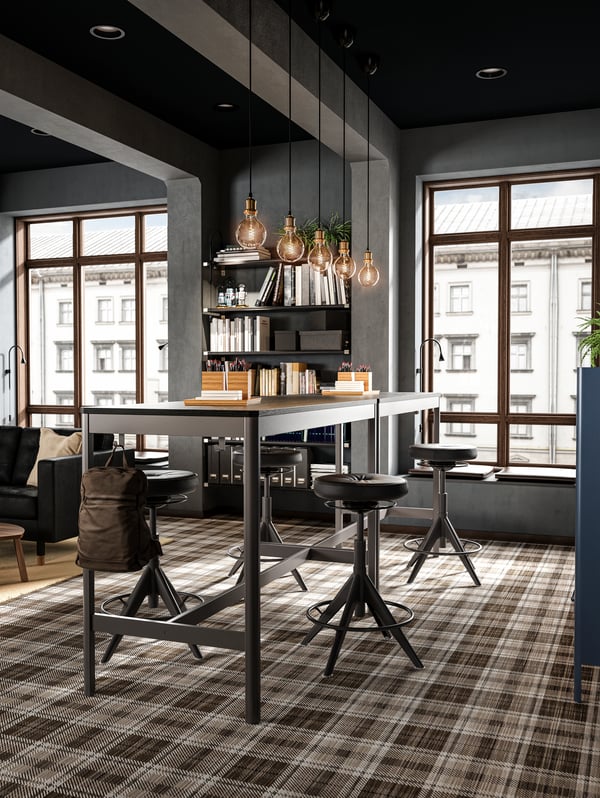 Deux tables hautes mises côte à côte, huit tabourets assis-debout, cinq suspensions en verre et des tablettes avec des livres.