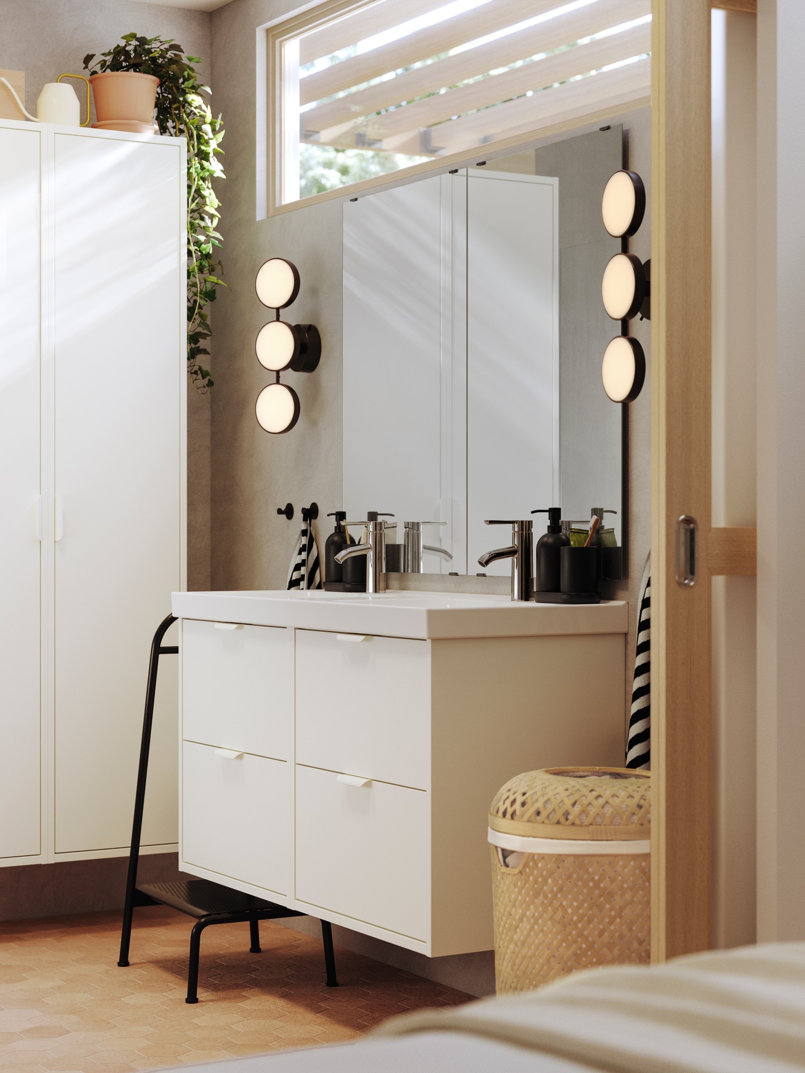 A bathroom has white HAVBÄCK bathroom furniture, black KABOMBA LED wall lamps and a BÄSINGEN step stool in anthracite.