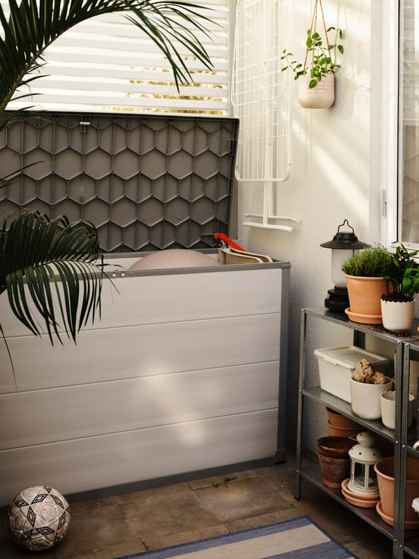 A light grey VRENEN storage box with the lid open, a white MULIG drying rack hanging on a wall, plus shelving with plants.