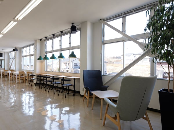 窓際に木製カウンターテーブルと黒いスツールを並べたワークスペース。手前に一人掛けチェアと観葉植物が置かれている。