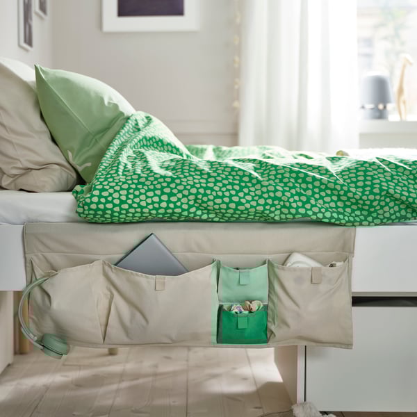 Beige MÖJLIGHET-Bett-Tasche mit Tablet und Zubehör an Bett mit grüner gemusterter Bettwäsche.