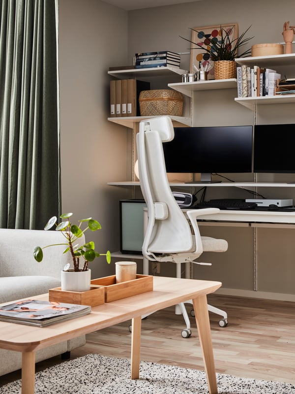 Elegantna domača pisarna z bež stenami in lesenimi tlemi. JÄRVFÄLLET gaming stol stoji poleg pisalne mize z dvema zaslonoma.