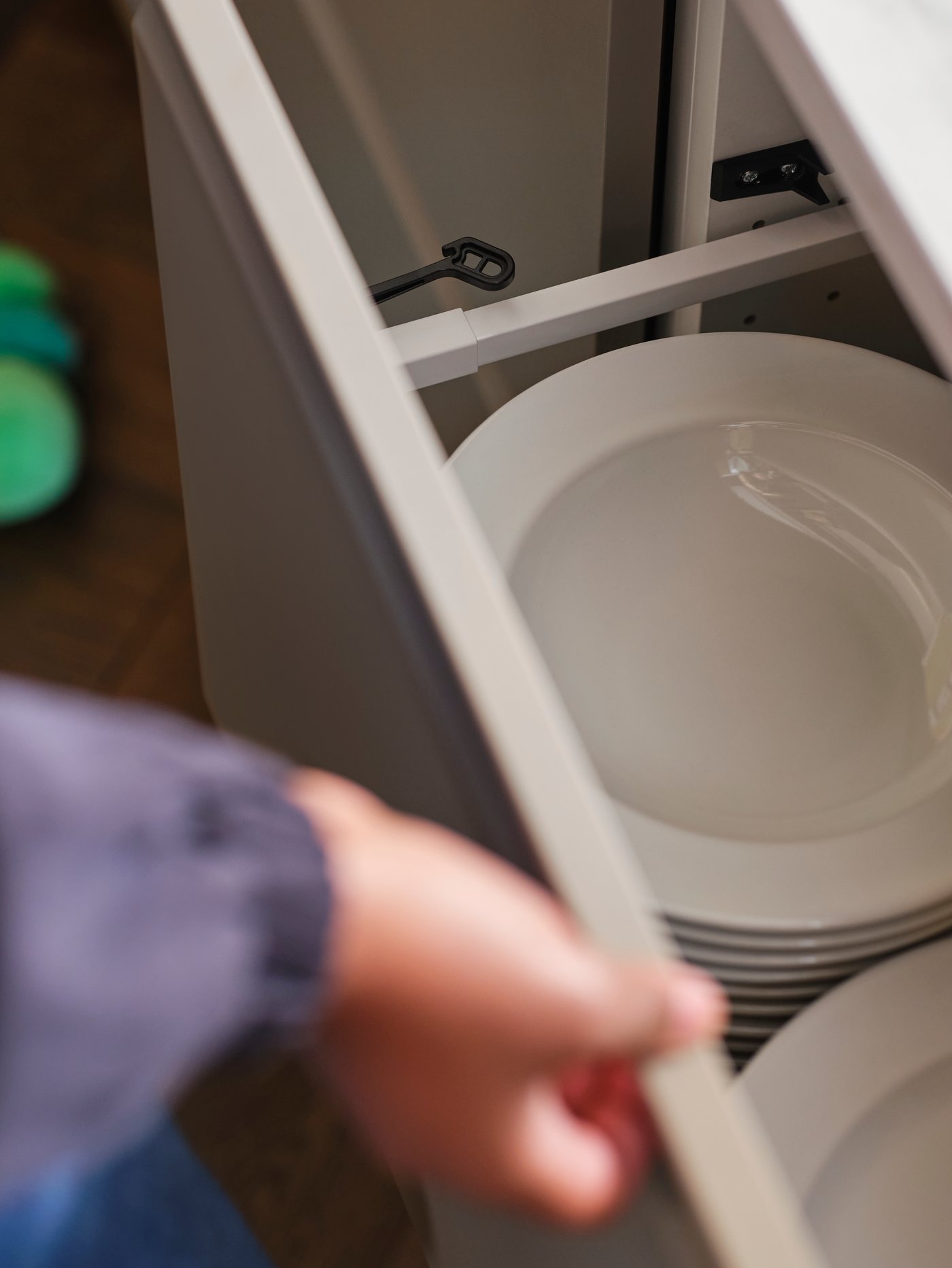 יד פותחת מגירת מטבח עם מנעול למגירות/ארונות מטבח UTRUSTA בשחור, ובפנים צלחות עמוקות בצבע לבן.