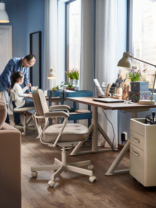A man and a child in a room with desks in ash veneer next to the windows, HEKTAR work lamps and beige ALEFJÄLL office chairs.