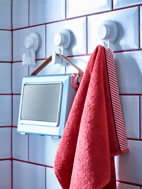 Close-up of modern bathroom tiled wall with three white suction cup hooks, a red towel and a box with brown leather strap. 