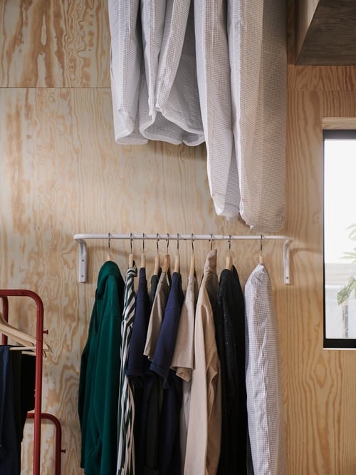 Bedroom with white clothes racks mounted on the wall, clothes on hangers, placed on the racks, red clothes rack with hangers.