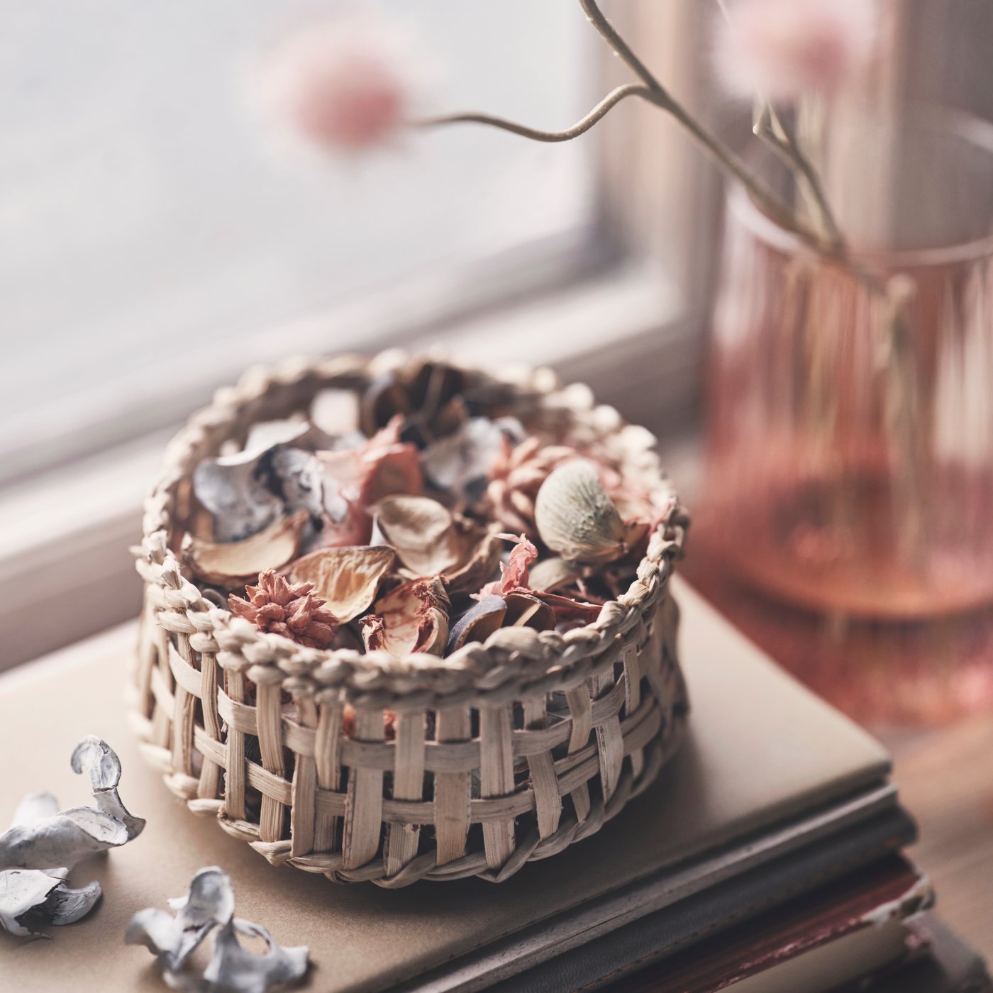 A hand-braided VÅRDANDE basket, made from banana fibre, is filled with potpourri in front of a window.