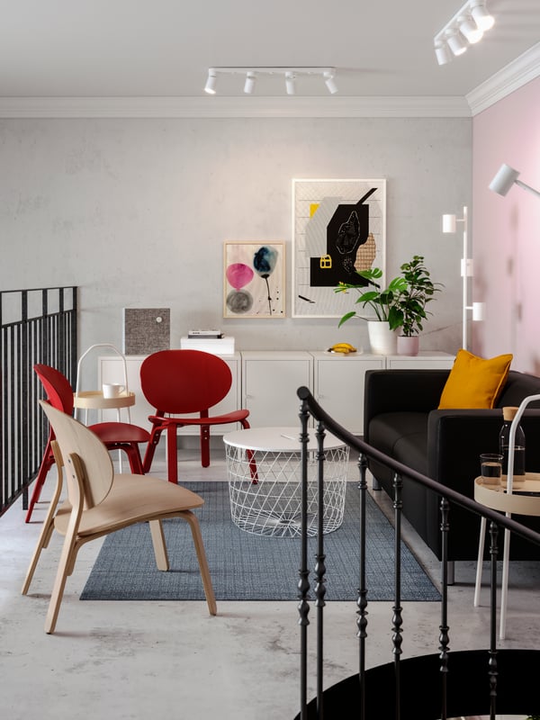 A lounge area with a black sofa, red easy chairs, colorful art on the wall, a white storage table.
