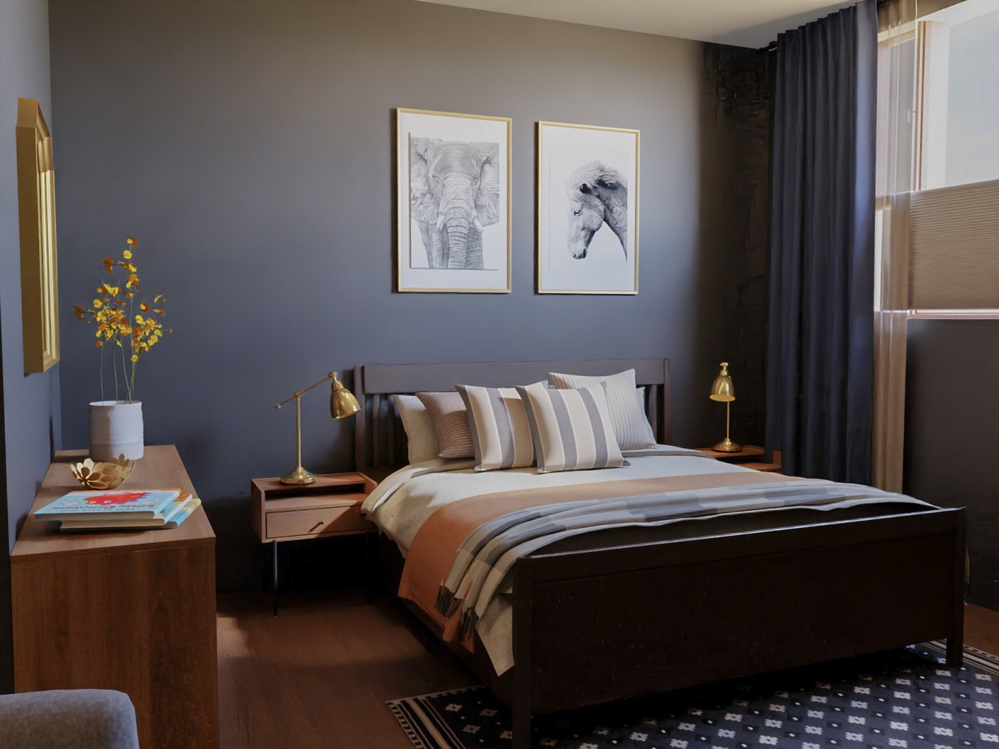 Teil eines Hotelzimmers. Blick auf ein Doppelbett mit zwei Nachttischen und Beleuchtung. An der Wand über dem Bett zwei große Bider. links neben dem Bett eine Kommode, darauf dekorative Gegenstände.