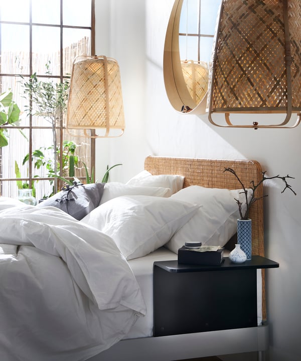 Ein weißes Bett steht in einer Ecke neben einer Fensterfront. Daneben steht eine große Stehlmape.