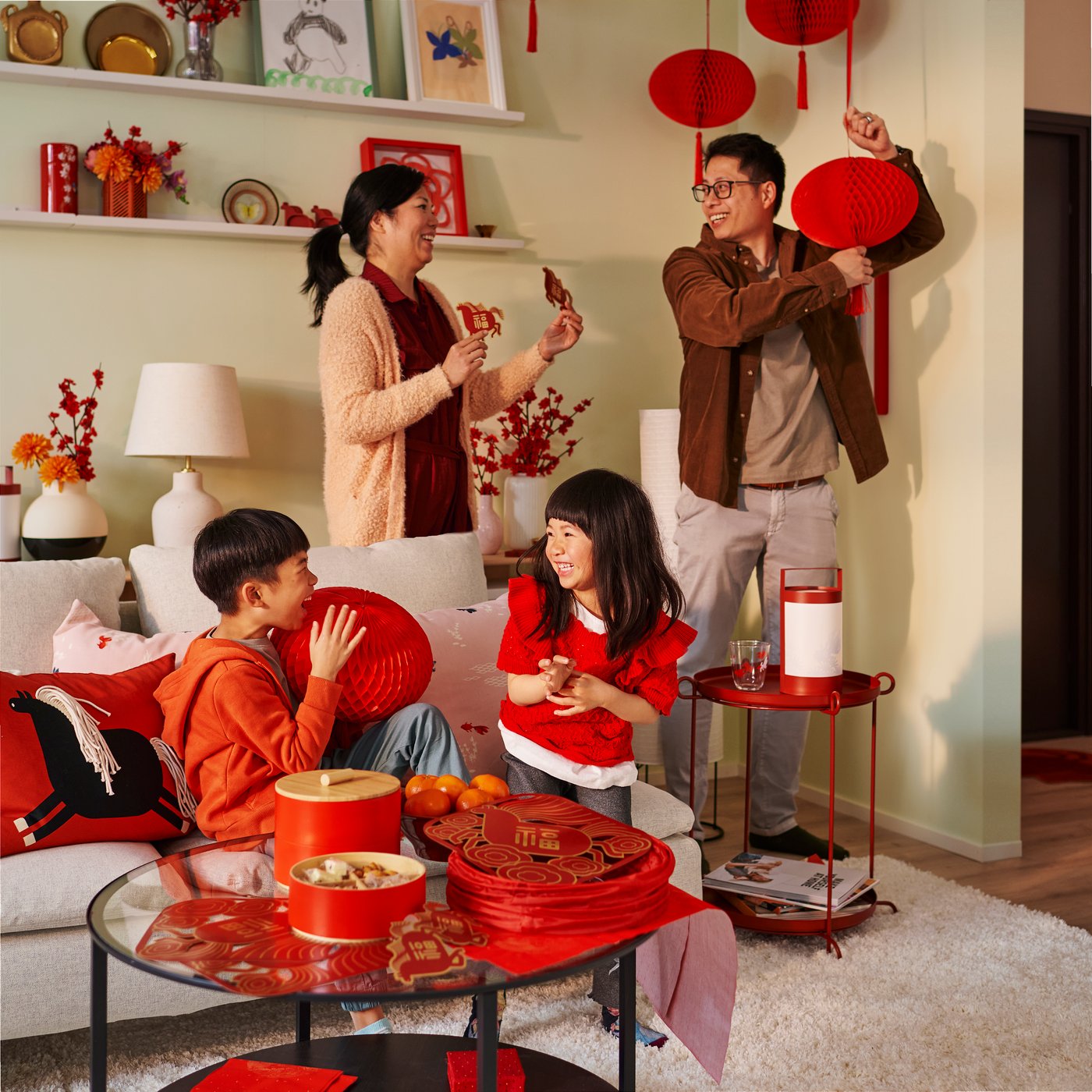A vibrant living room with some red FÖSSTA LED lanterns, cosy decorations, and a family enjoying a festive moment together.