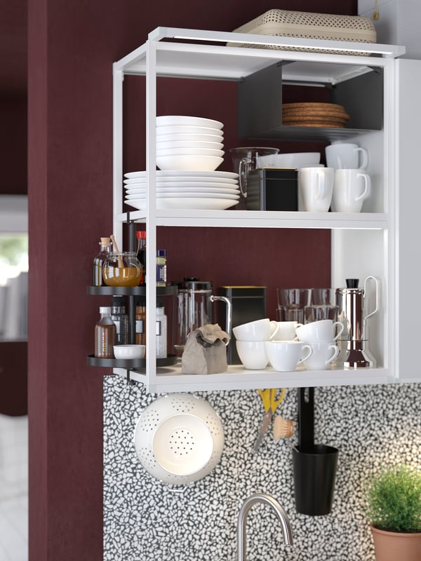 A white ENHET open shelf holding cups and kitchenware against a dark red wall with a black and white LYSEKIL panel below.