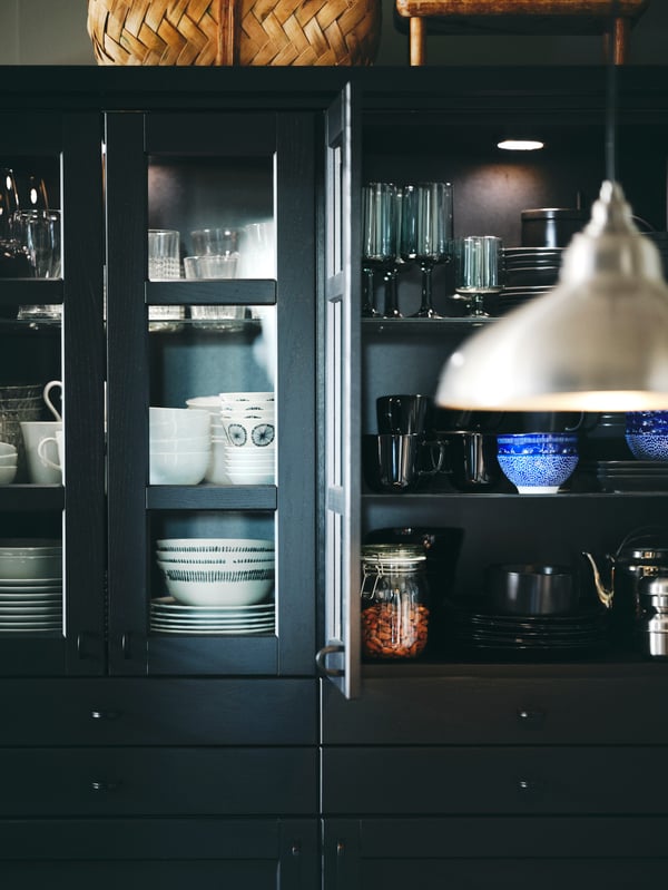 Glassware and dinnerware including white/patterned FRIKOSTIG bowls in cabinets with black stained LERHYTTAN glass doors.
