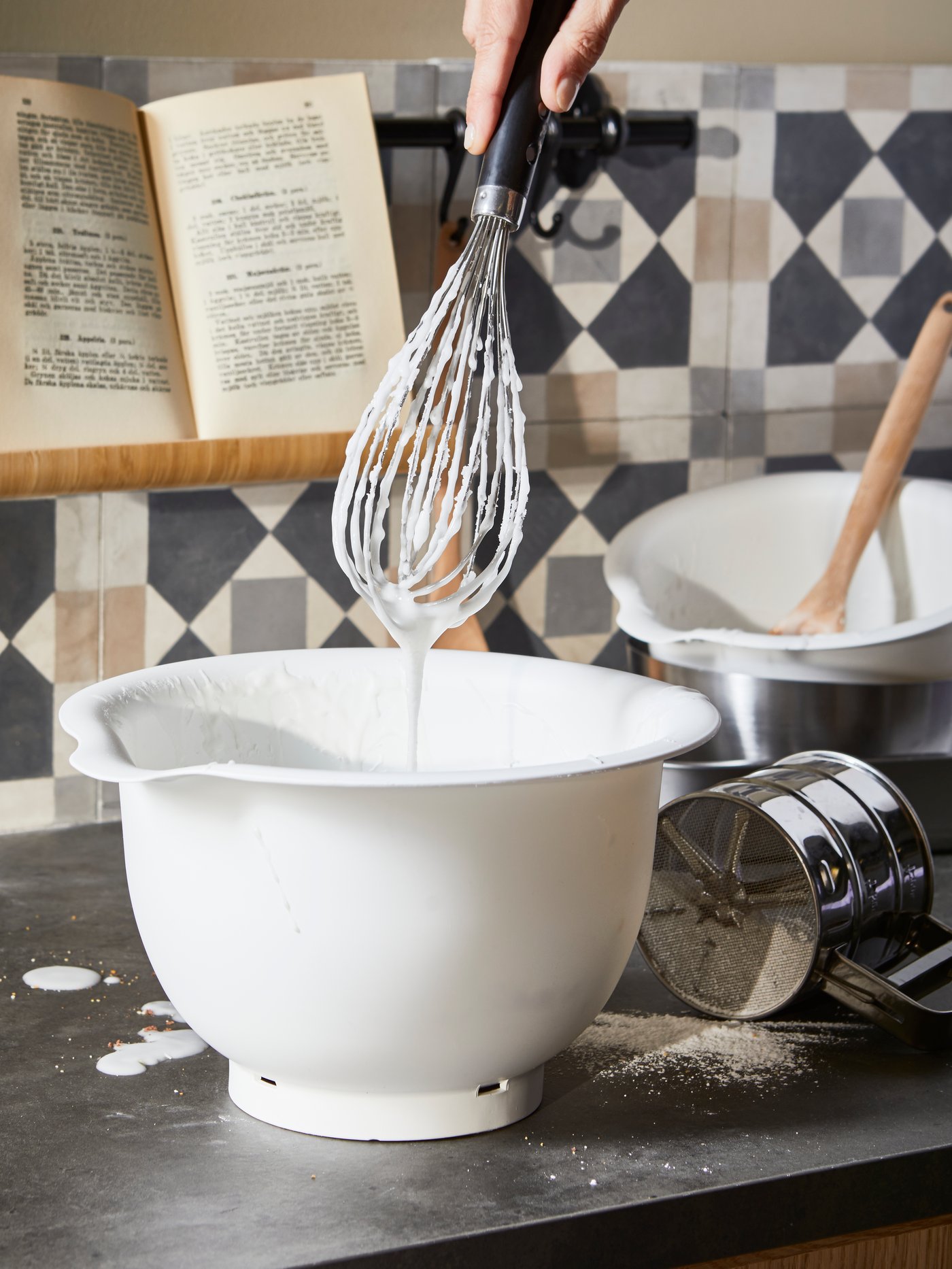 Ruka drží metličku KEA 365+ nad bílou mísou VISPAD, která stojí na kuchyňské lince.